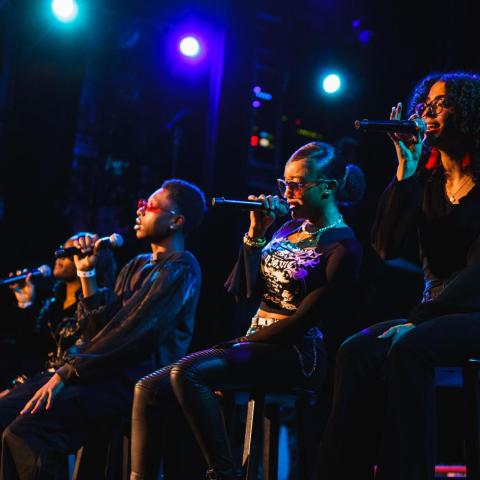 Four High School Academy vocalists sit on stools, each holding a microphone on the Berklee Performance Stage
